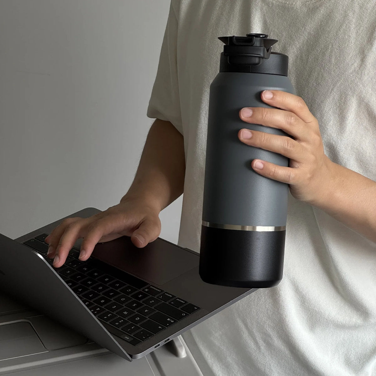 Person holding a black water bottle while using a laptop.