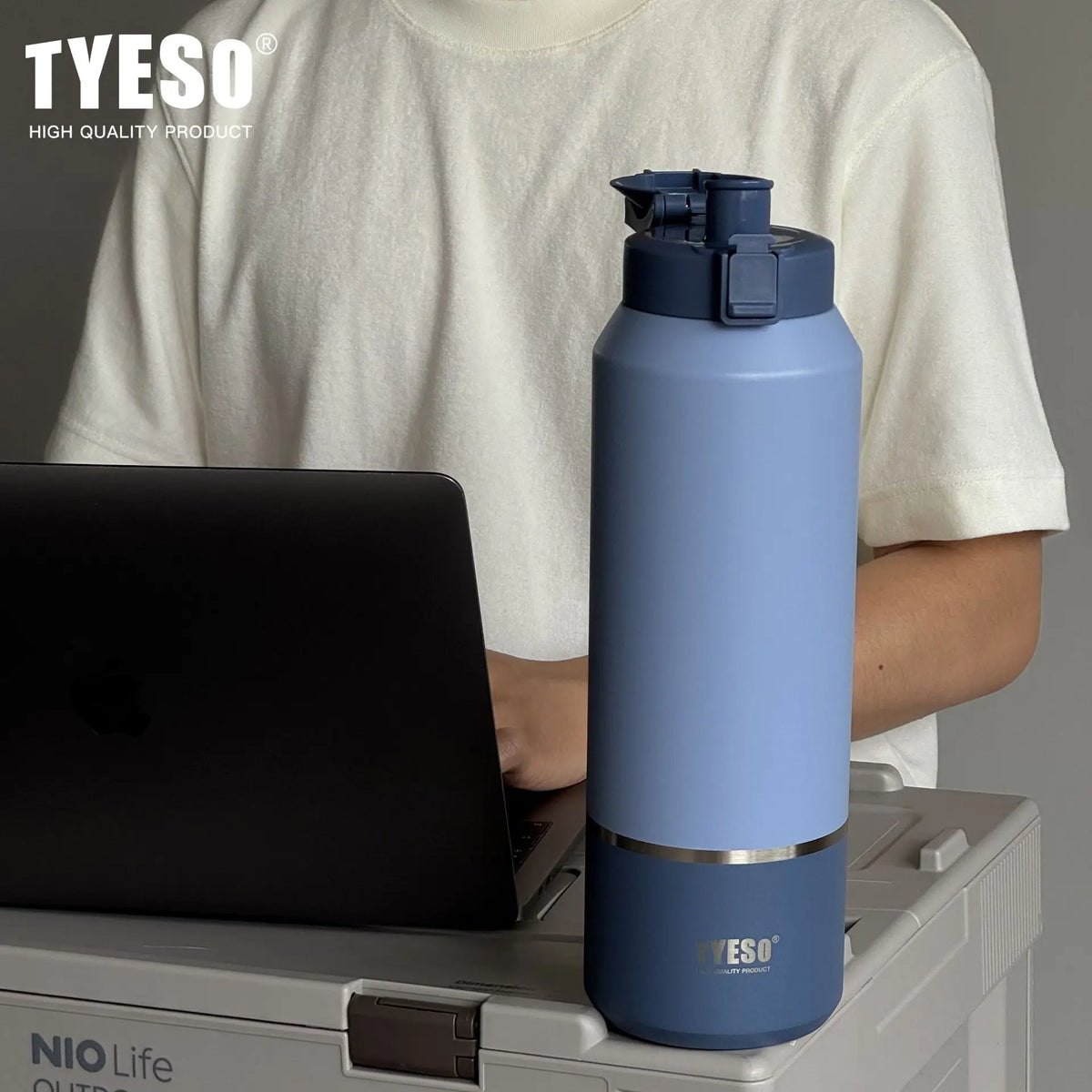 Blue water bottle with 'TYESO' branding on a surface next to a person using a laptop.