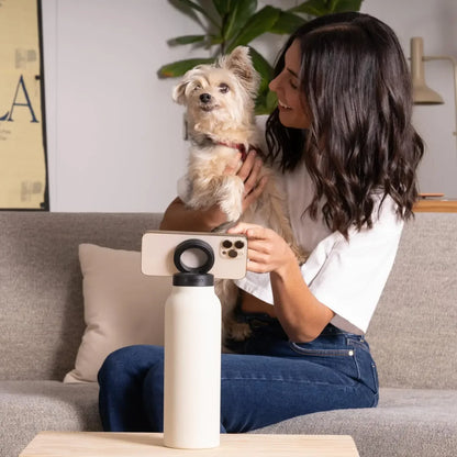 Woman holding a small dog and taking a photo with a smartphone on a white water bottle stand.