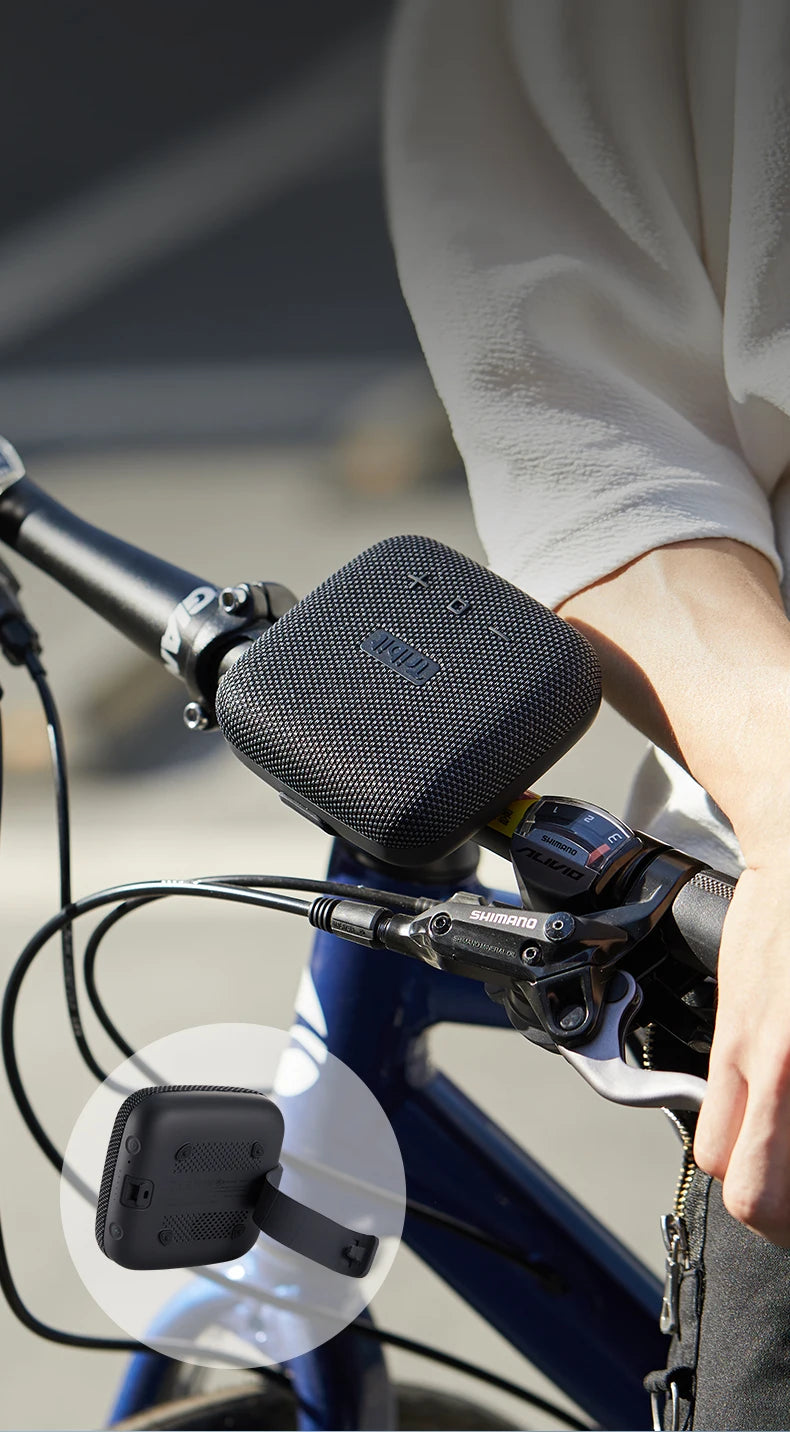 Person holding a black portable speaker attached to a bicycle handlebar