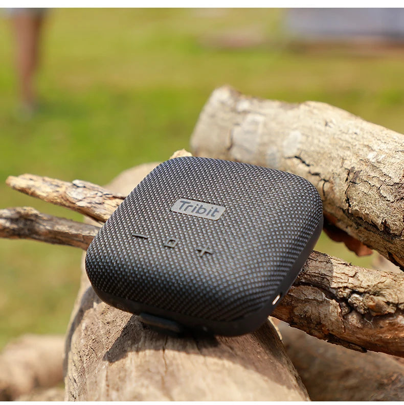 Black Tribit portable speaker on a wooden log with a blurred natural background