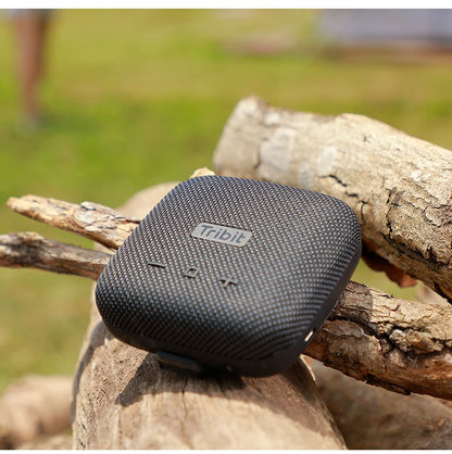 Black Tribit portable speaker on a wooden log with a blurred natural background