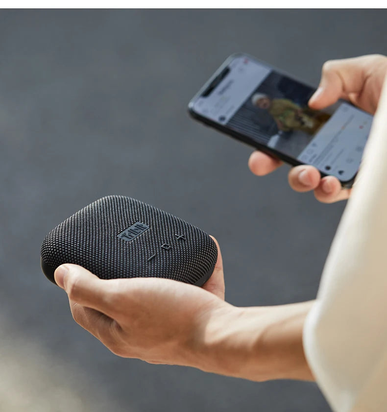 Person holding a black portable speaker and using a smartphone with a blurred background