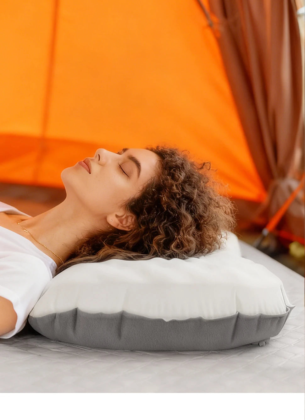 Woman lying on a gray inflatable pillow in front of an orange tent.