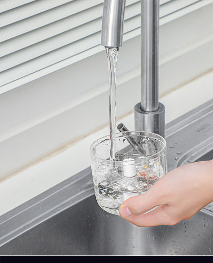 Clear glass with water being poured from a faucet into it, with a hand holding the glass.